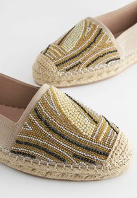 Beaded espadrilles met een beige stof bovenkant, met een decoratief patroon van gouden, zwarte, zilveren en witte kralen, en een jute zool.