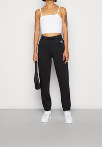 Svarta sweatpants med elastiska mudd, dragsko i midjan, sidofickor och en vit Nike-logotyp. Matchas med en vit cropped top och vita sneakers.