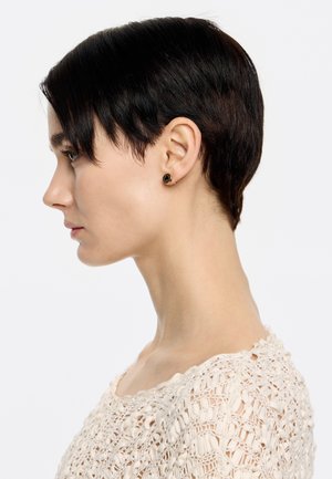 Gold-tone stud earrings with black gemstone detail, circular shape, set on a short-haired individual wearing a cream knit top.