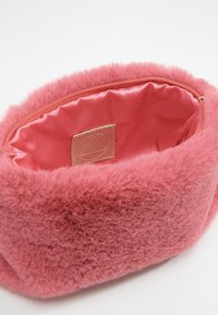 Trousse de maquillage ronde et moelleuse en fausse fourrure rose clair, avec un intérieur lisse et satiné. Fermeture éclair et logo embossé à l'intérieur.