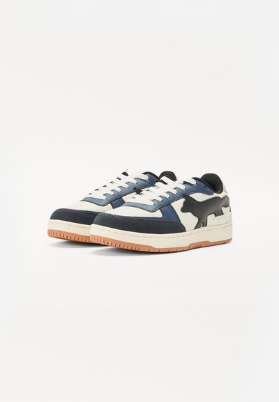 Zapatillas multicolores con un diseño en blanco, azul marino y negro. Presentan una parte superior texturada, suela de goma y un notable detalle de silueta de gato negro.