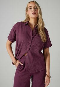 Camicia a maniche corte con bottoni e pantaloni abbinati in un profondo color prugna. Tessuto testurizzato con una vestibilità rilassata. La camicia presenta una tasca e bottoni.