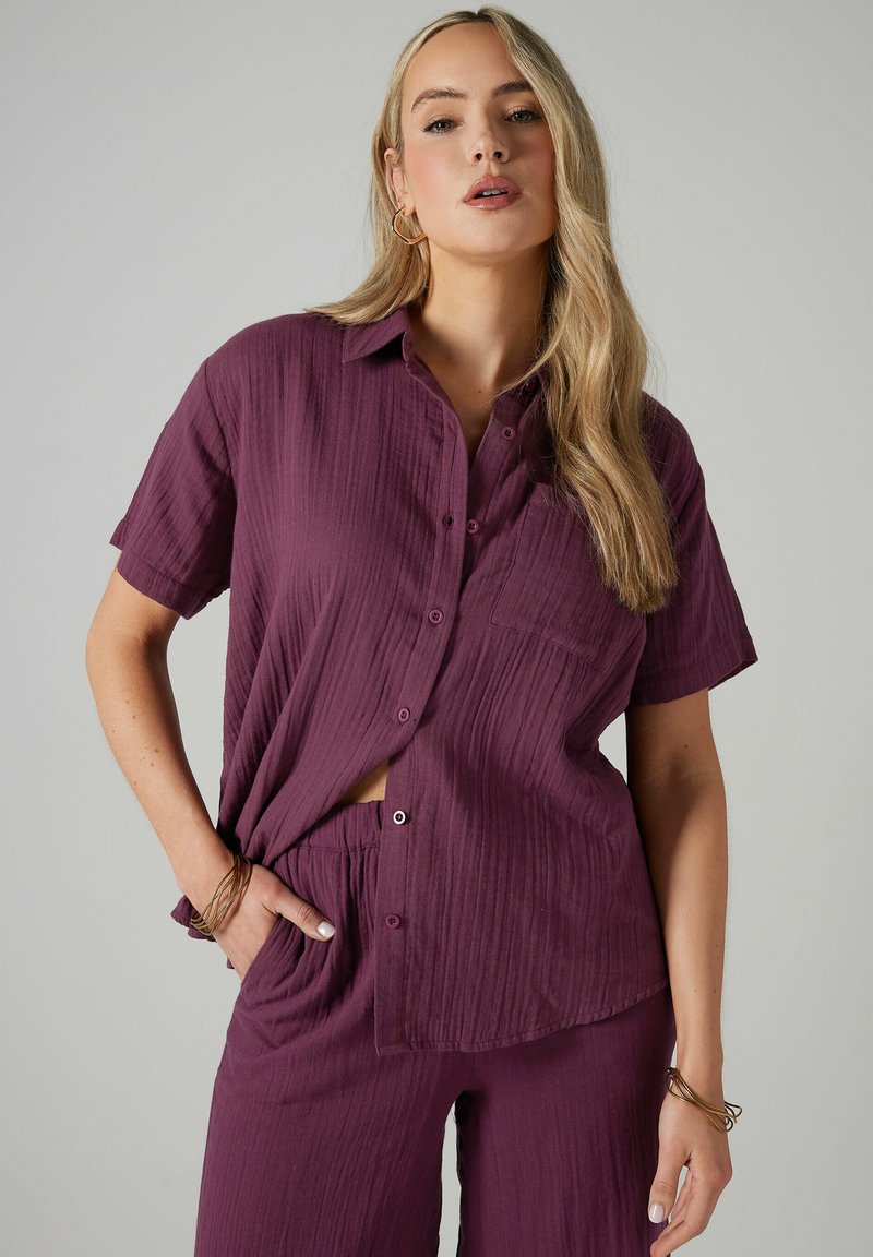 Camicia a maniche corte con bottoni e pantaloni abbinati in un profondo color prugna. Tessuto testurizzato con una vestibilità rilassata. La camicia presenta una tasca e bottoni.