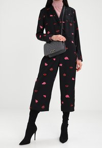 Černý overal s dlouhými rukávy a širokými nohavicemi, zdobený růžovými a červenými otisky rtů. Kombinován s šedou prošívanou kabelkou a černými botami na jehlovém podpatku.