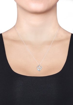 Collier en forme de cœur en argent avec l'inscription « Mom » et petit pendentif en pierre précieuse porté au cou d'une femme avec un haut noir.