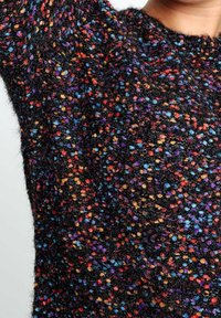 Svart tröja med texturerat stickat mönster och flerfärgade prickar i röd, blå, orange och lila, vilket skapar ett livfullt mönster.