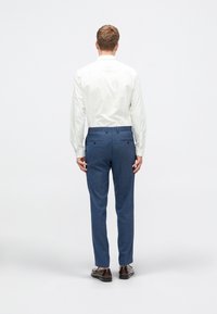 Pantaloni bleumarin, croiți, cu un țesut texturat, două buzunare la spate, asortați cu o cămașă albă cu mânecă lungă și pantofi maro.