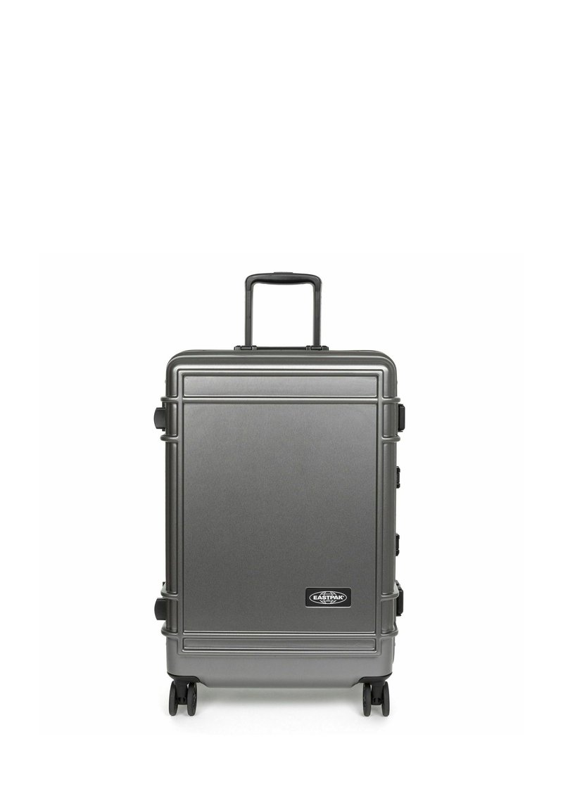 Valigia rigida grigia con finitura testurizzata, manico telescopico e quattro ruote scorrevoli; presenta un logo del marchio nella parte inferiore.