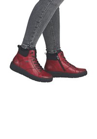 Des chaussures montantes en cuir rouge avec des accents noirs, un système de laçage et une fermeture éclair, une semelle rembourrée et une texture lisse, idéales pour un usage décontracté.