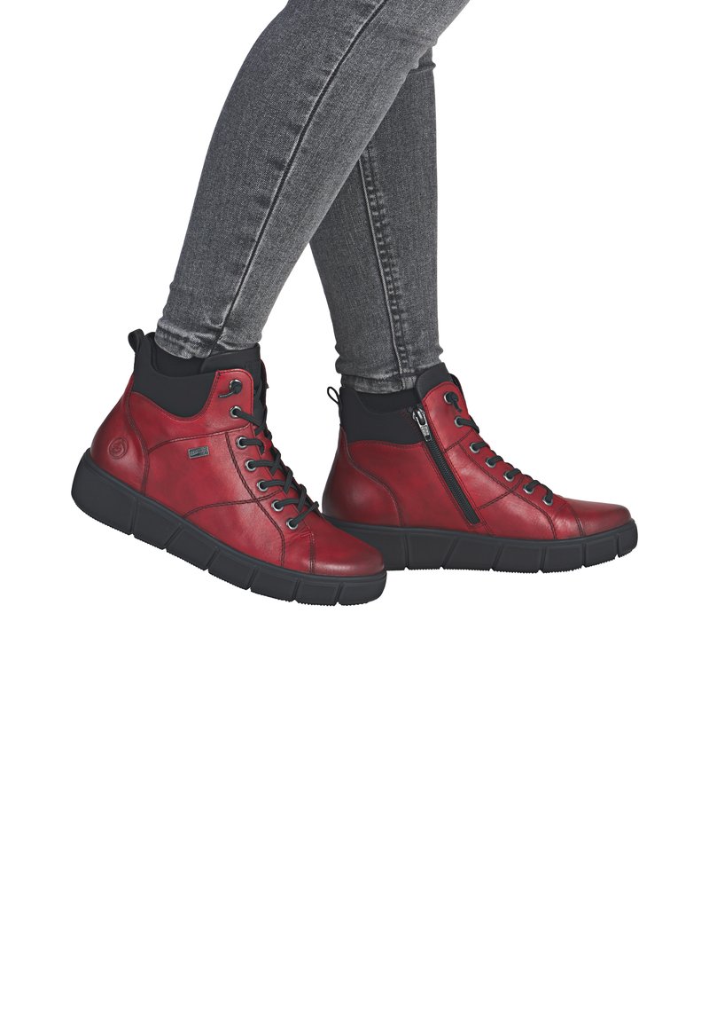 Des chaussures montantes en cuir rouge avec des accents noirs, un système de laçage et une fermeture éclair, une semelle rembourrée et une texture lisse, idéales pour un usage décontracté.