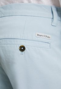 Shorts en coton bleu clair avec une poche arrière à bouton et une étiquette portant la mention "Marc O'Polo". Texture lisse et design ajusté.