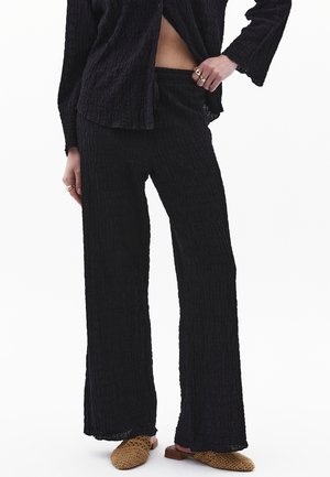 Černý texturovaný dvoudílný outfit se širokými kalhotami a volným košilovým topem. Ozdobený jemnými vráskami a uvolněnými rukávy.