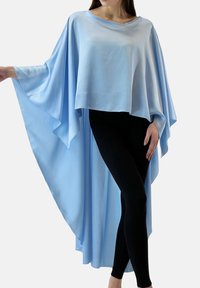 Lichtblauwe, vloeiende cape van gladde stof, met brede mouwen en een asymmetrische zoom, gecombineerd met zwarte legging.