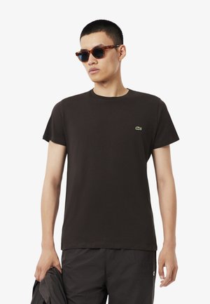 T-shirt en coton noir à manches courtes et col rond ; présente un petit logo brodé vert sur la poitrine. Le modèle tient une veste.