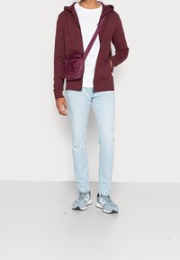 Burgundowa rozpinana bluza, biała koszulka, jasnoniebieskie dżinsy z przetarciami, czarno-szare trampki, z małą fioletową torbą na ramię.