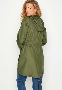 Giacca leggera color verde oliva con cappuccio e vita elastica, caratterizzata da una texture liscia e da un design casual, che scende sotto i fianchi.