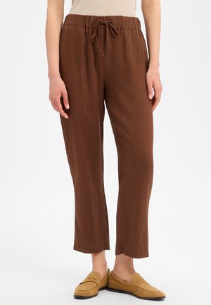Bruine losse linnen broek met trekkoord in de taille, gedragen met beige suède loafers bij een staand persoon.