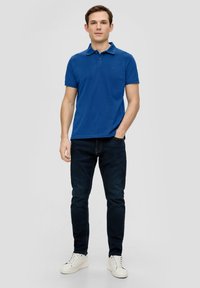 Polo blu in cotone, abbinato a jeans blu scuro e sneakers bianche. Design semplice con colletto e maniche corte.