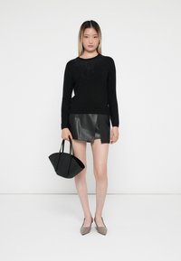 Pull en maille noir avec des détails scintillants, associé à une mini-jupe en cuir noir, un sac à main noir et des ballerines pointues en taupe.