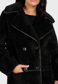 Cappotto nero doppiopetto realizzato in tessuto testurizzato, caratterizzato da un ampio colletto, dettagli in pelle e grandi bottoni dalla finitura liscia.