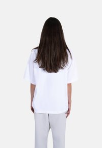 Hvit oversized t-skjorte med korte ermer, glatt tekstur, rund hals og rett nederkant, kombinert med lysegrå bukser.