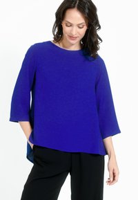 Top blu loose-fit con maniche a tre quarti e scollo rotondo, realizzato in tessuto liscio. Presenta fessure laterali e un orlo dritto.