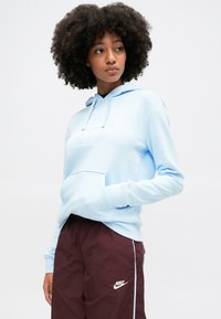 Svetlomodrá mikina s kapucňou a predným vreckom, so bielym logom, v kombinácii s vínovými teplákmi s bočnými pruhmi a logom na nohe.