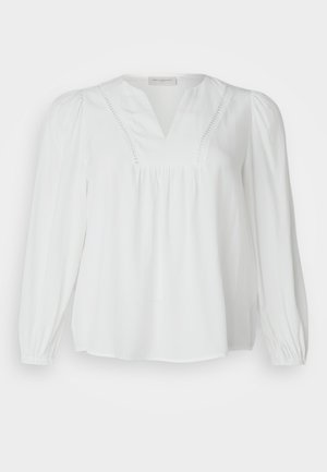 Valkoinen paita, jossa on V-kaula-aukko, laskostettu vartalo ja pitkät hihat. Valmistettu kevyestä kankaasta, jossa on hienovaraista koristekirjontaa kaula-aukossa.