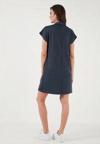 Short navy dress with cap sleeves, featuring a back seam and a relaxed fit. Paired with white sneakers for a casual look.
