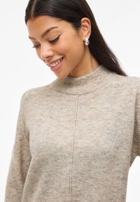 Bézs kötött pulóver magas bordázott gallérral, finom melírozott mintával és egyszerű, letisztult dizájnnal.