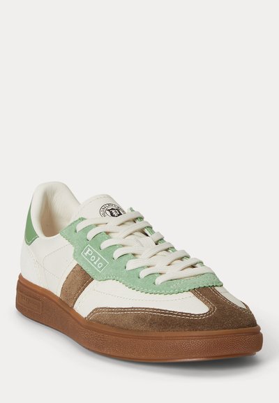 Λευκό δερμάτινο αθλητικό παπούτσι με καφέ σουέντ λεπτομέρειες, πράσινο σουέντ προστατευτικό κορδονιών, λογότυπο Polo, λευκά κορδόνια και καφέ λαστιχένια σόλα, στραμμένο προς τα δεξιά.