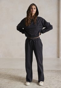Donkergrijze cropped hoodie met een trekkoordcapuchon, gecombineerd met losse donkergrijze joggingsbroek. Beide gemaakt van zachte, gestructureerde stof.