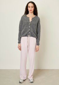 Šedý vlněný cardigan s kulatým výstřihem a knoflíky, v kombinaci se světle růžovými volnými kalhotami. Má uvolněný střih a měkkou texturu.