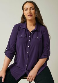 Purple, long-sleeve button-up shirt with two front pockets, silver buttons, and rolled sleeves. Soft fabric and relaxed fit.
