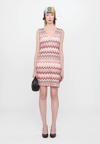 Patterned sleeveless dress featuring a chevron design in pink, brown, and cream tones, paired with a black clutch handbag and high heels.