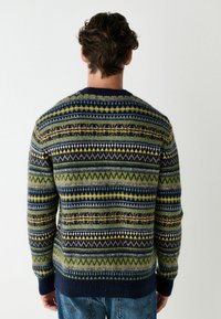 Kootud sviiter, millel on mitmevärviline geomeetriline muster rohelises, navy-sinises ja kollases, ribaga kaeluse ja äärtega.
