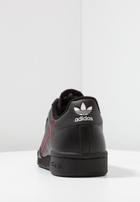 Sorte lædersneakers med røde accenter, en struktureret overflade og et hvidt Adidas-logo på hælen. Rundt design med lav profil.