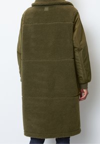 Olivgrön lång kappa med en plyschig, strukturerad fleecebak och släta nylonärmar. Har en krage och ribbade manschetter.