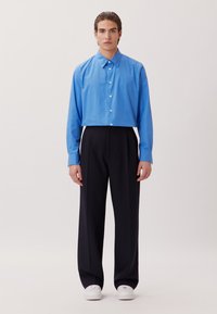 Blaue Hemdbluse mit langen Ärmeln, kombiniert mit schwarzen weiten Hosen und weißen Sneakers. Glatte Stoffqualität und lässige Passform.