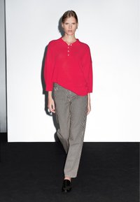 Maglione polo rosso lavorato a maglia con pattina dei bottoni, abbinato a pantaloni a righe bianche e nere. Il modello indossa mocassini neri.