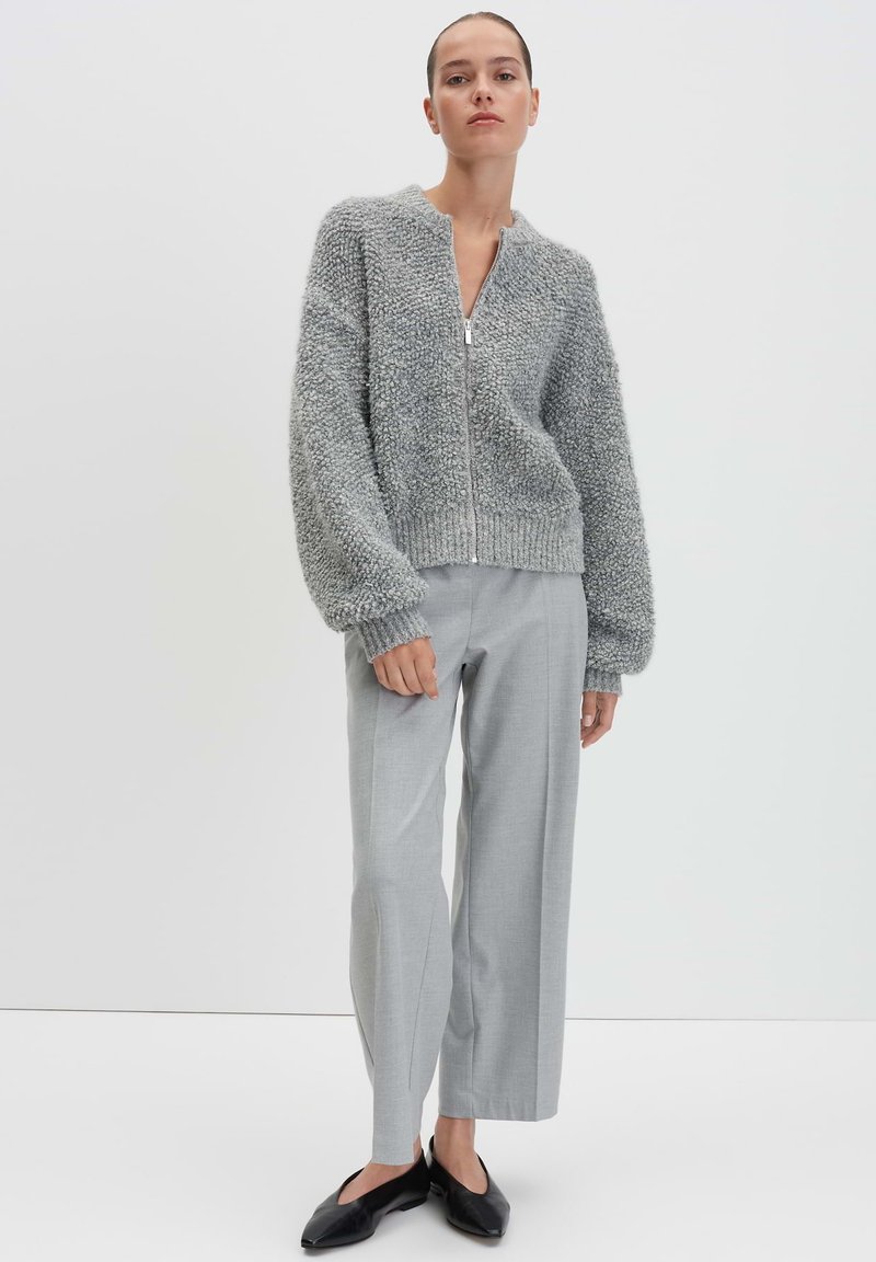 Maglione grigio con zip, dalla consistenza particolare e maniche oversize, abbinato a pantaloni larghi grigi chiari e ballerine nere. Design semplice e moderno.