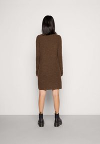 Brown knitted long-sleeve dress with a straight fit, ending above the knees. Paired with black ankle boots featuring a thick sole.
