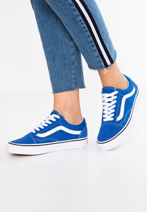 Jalat, joissa sinivalkoiset matalakärkiset tennarit ja lyhytvartiset siniset farkut, joissa mustavalkoiset sivuraitarit.