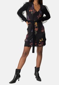 Black floral dress with polka dots, V-neck, lace sleeves, and scalloped hem. Includes a black belt to accentuate the waist. Worn with black ankle boots.