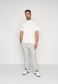 Calças de moletão cinza claro, t-shirt branca com um pequeno logótipo em texto e ténis brancos. Ajuste casual com tecido macio e cintura elástica.