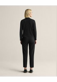 Musta neulepusero pitkillä hihoilla, yhdistetty räätälöityihin mustiin housuihin ja mustiin kenkiin. Yksinkertainen muotoilu, sileä pinta ja vartalonmyötäinen istuvuus.