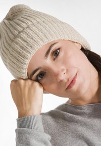 Berretto a coste color crema con una texture morbida, indossato da una persona in un maglione grigio chiaro, che mette in mostra il design e la vestibilità del cappello.