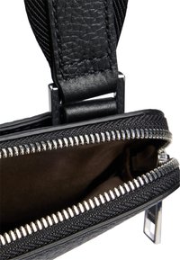 Czarna skórzana torba z teksturowanym wykończeniem, srebrnym zamkiem błyskawicznym i zamkiem, który odsłania brązowe wnętrze z materiału.