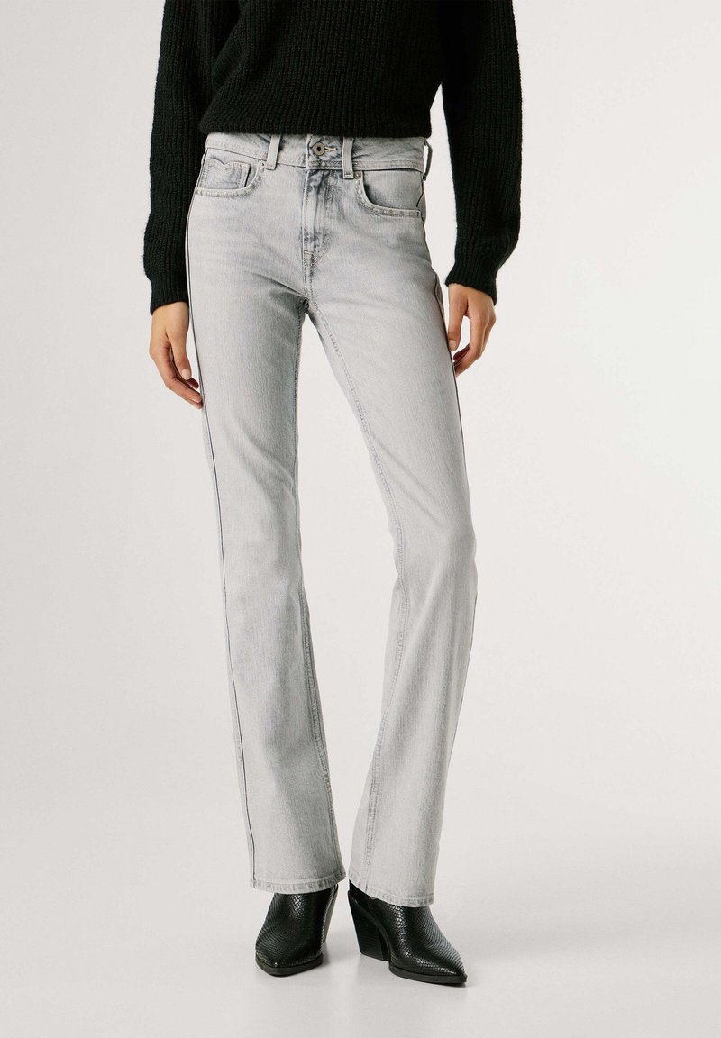 Ανοιχτό γκρι τζιν με ίσια γραμμή, πέντε τσέπες και κουμπί στο κλείσιμο. Φορεμένα με μαύρο πλεκτό πουλόβερ και μπότες με τακούνι.