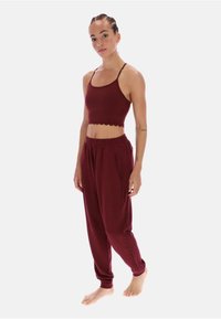 Bordeauxfarvet sportsæt med en kort top med bølget kant og løstsiddende joggingbukser med sidelommer og elastiske manchetter ved anklerne.